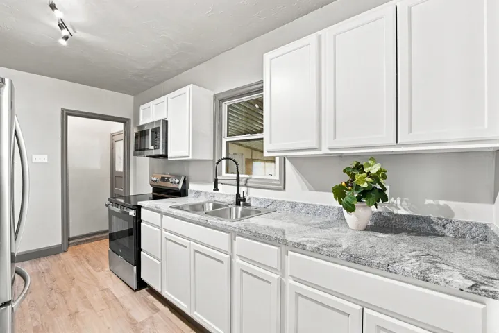 White shaker cabinetry, stainless steel appliances, dual basin sink, black gooseneck faucet, and wood-finish flooring