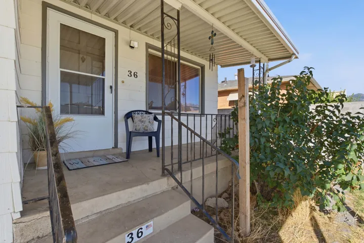Front porch featuring a white storm door, concrete steps, wrought iron railing, and white siding
