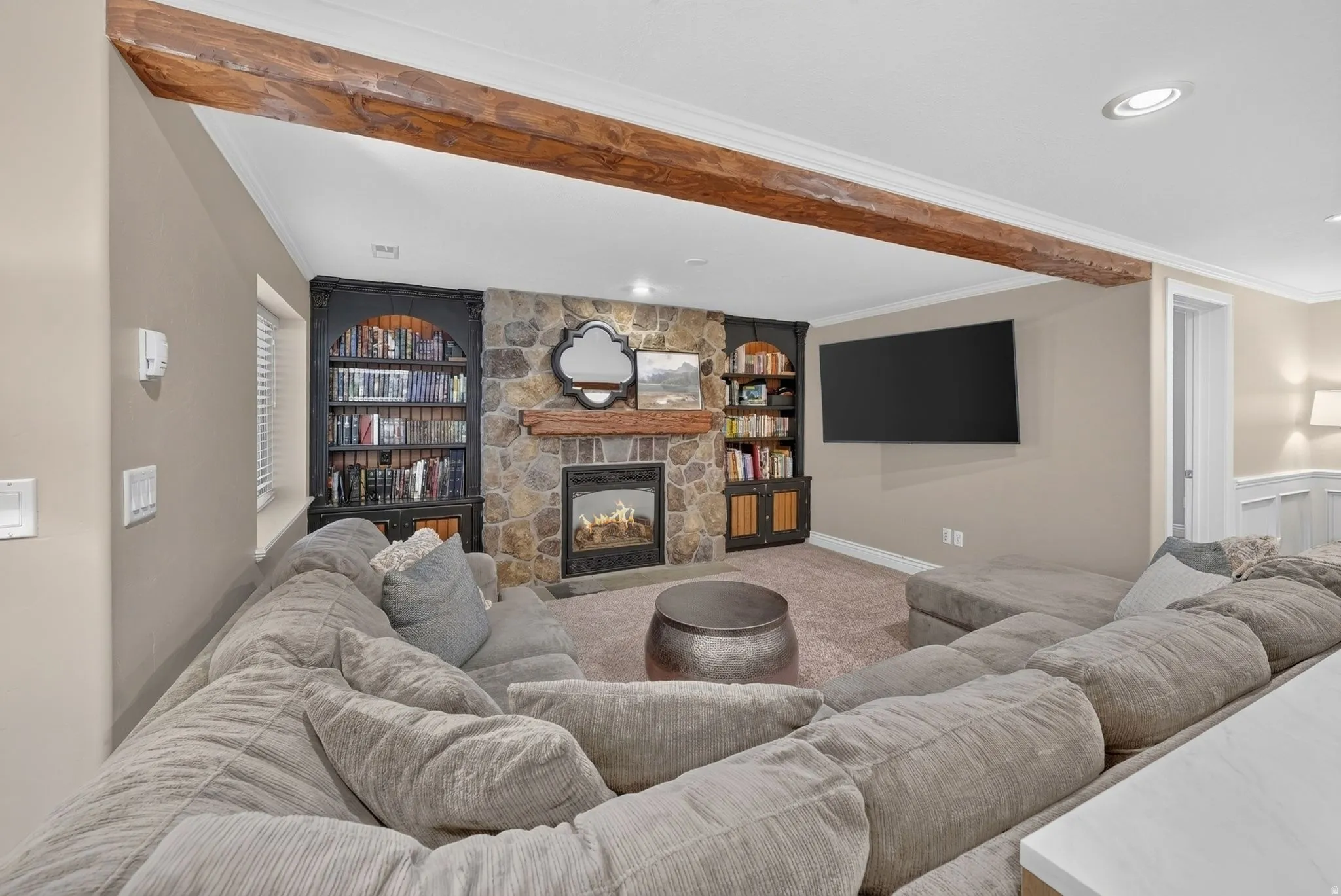 Stone-faced fireplace with a wood mantel, built-in shelving, wood-finish ceiling beam, and recessed lighting