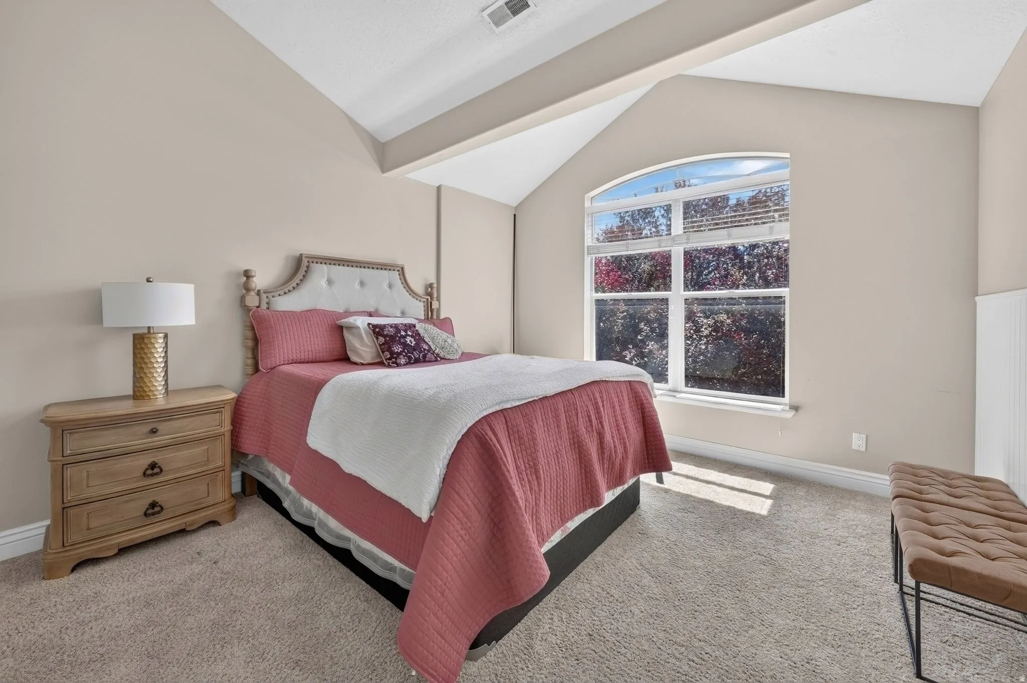 Arched window, vaulted ceiling, light neutral wall paint, carpet flooring, and white wainscoting