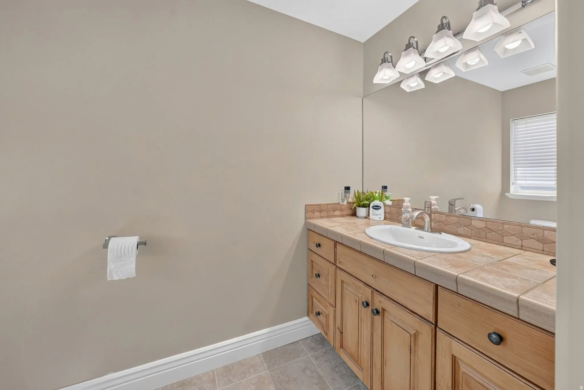 Wood-finish vanity with an integrated sink, tile countertop, and a full-width mirror