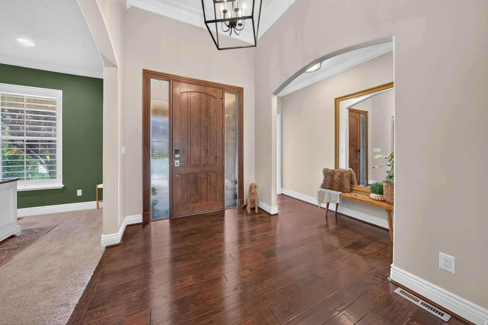 Wood-finish flooring, arched entryway, a substantial front door with sidelights, and crown molding