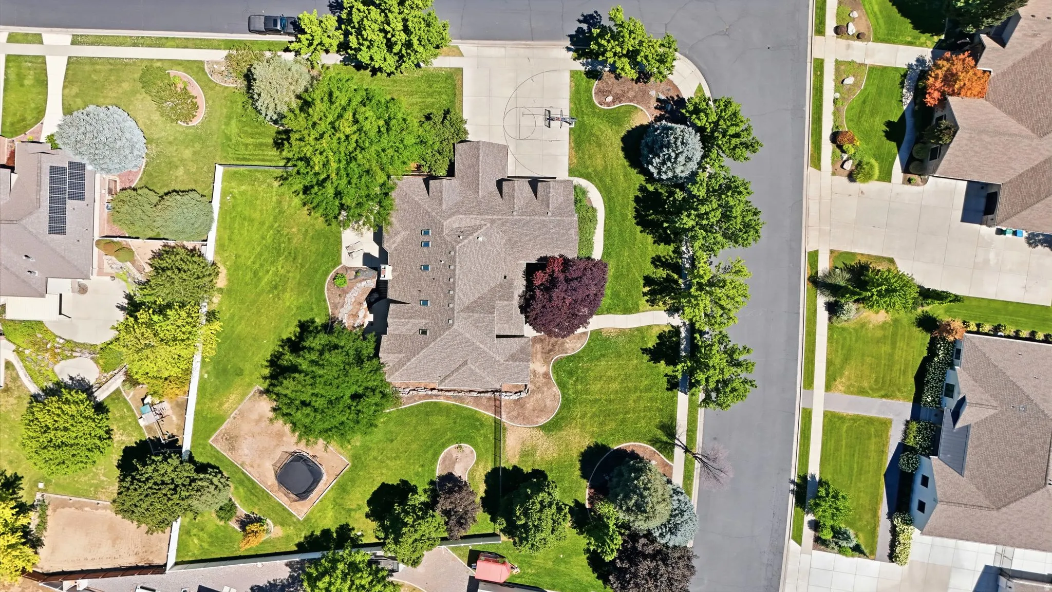 Aerial view showcasing a meticulously landscaped lot with mature trees, manicured lawn, defined hardscape pathways, and multiple garden beds