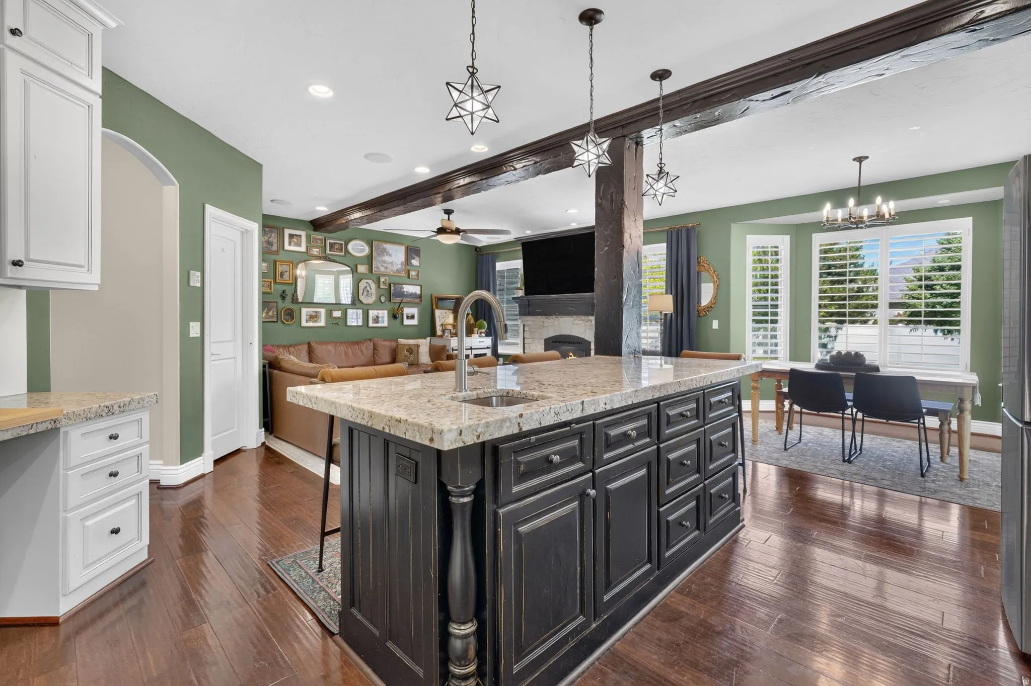 Kitchen island with granite countertop and integrated sink, dark wood-finish flooring, white built-in cabinetry, and exposed wood beams