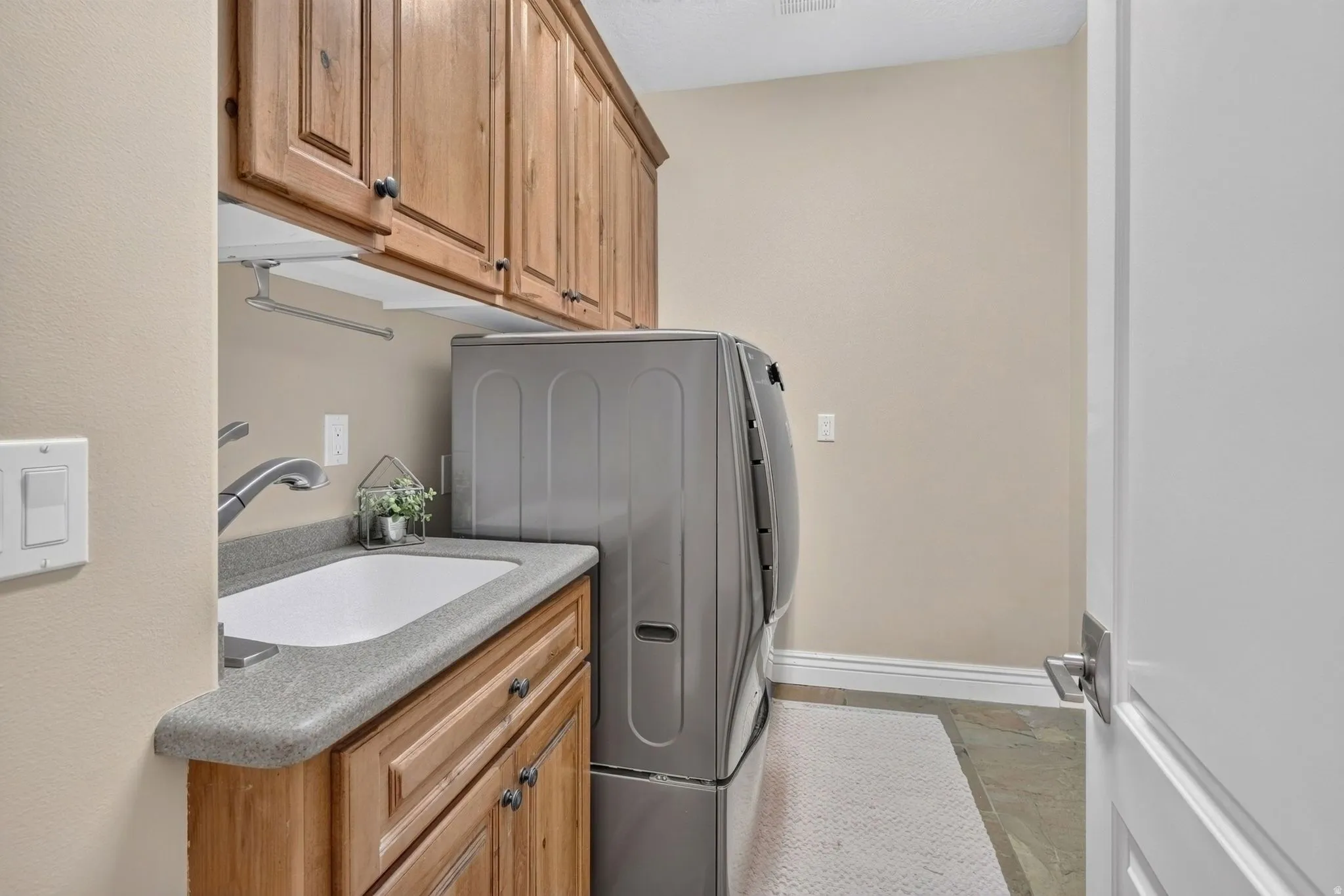 Laundry room with wood cabinetry, a built-in utility sink, and tile flooring