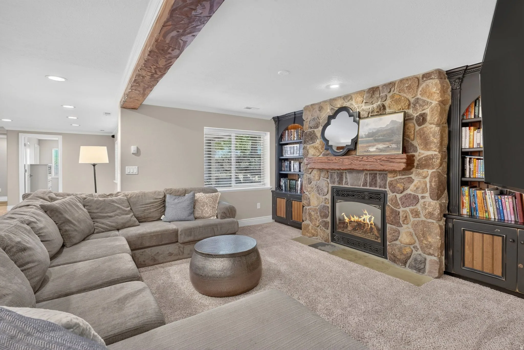 Stone-faced fireplace with a wood mantel, built-in shelving units, and exposed ceiling beam
