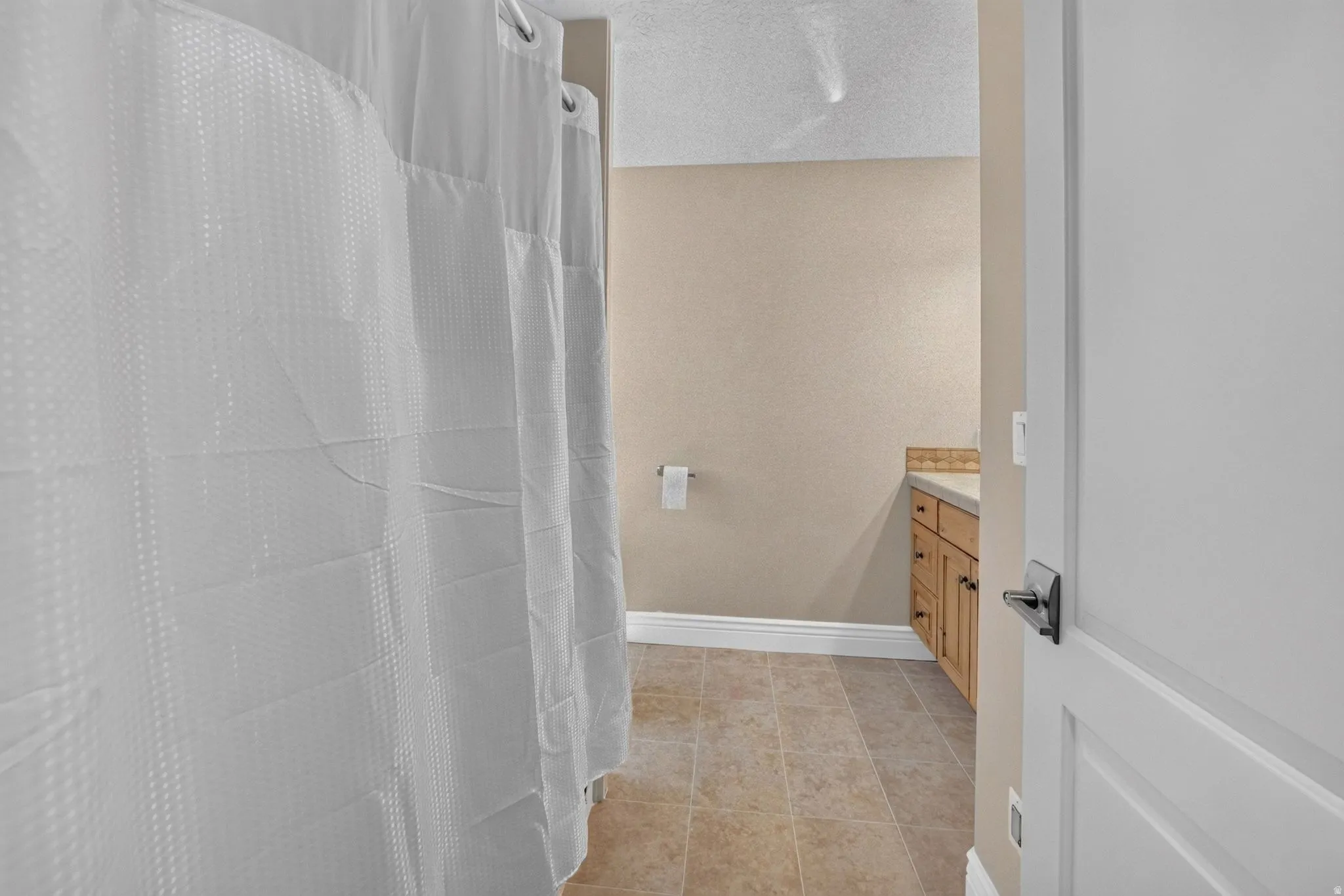 Tile flooring, wood-finish vanity with countertop, and a white interior door with dark hardware