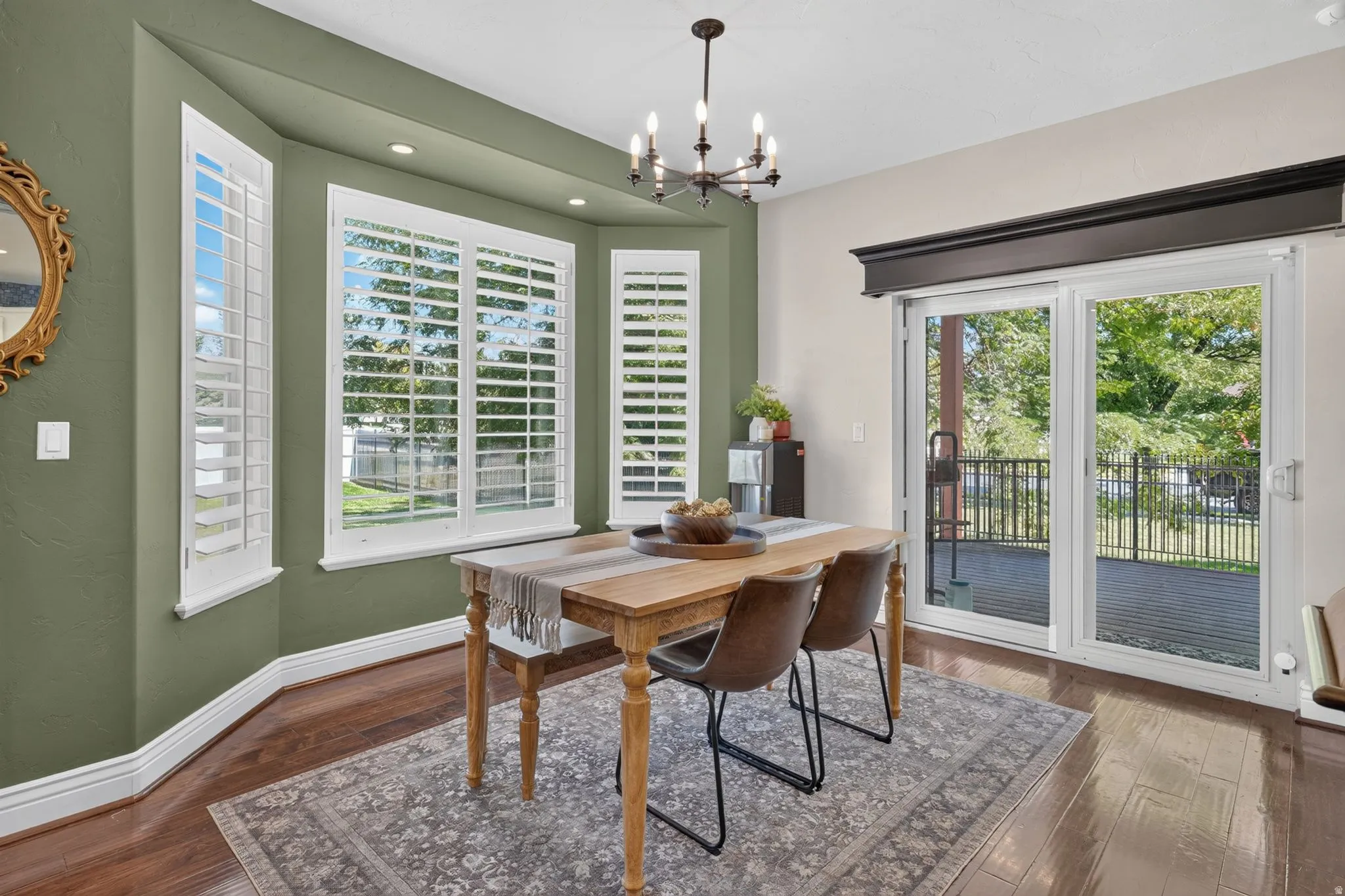 Bay window with plantation shutters, recessed lighting, wood-finish flooring, and sliding glass door leading to an outdoor deck