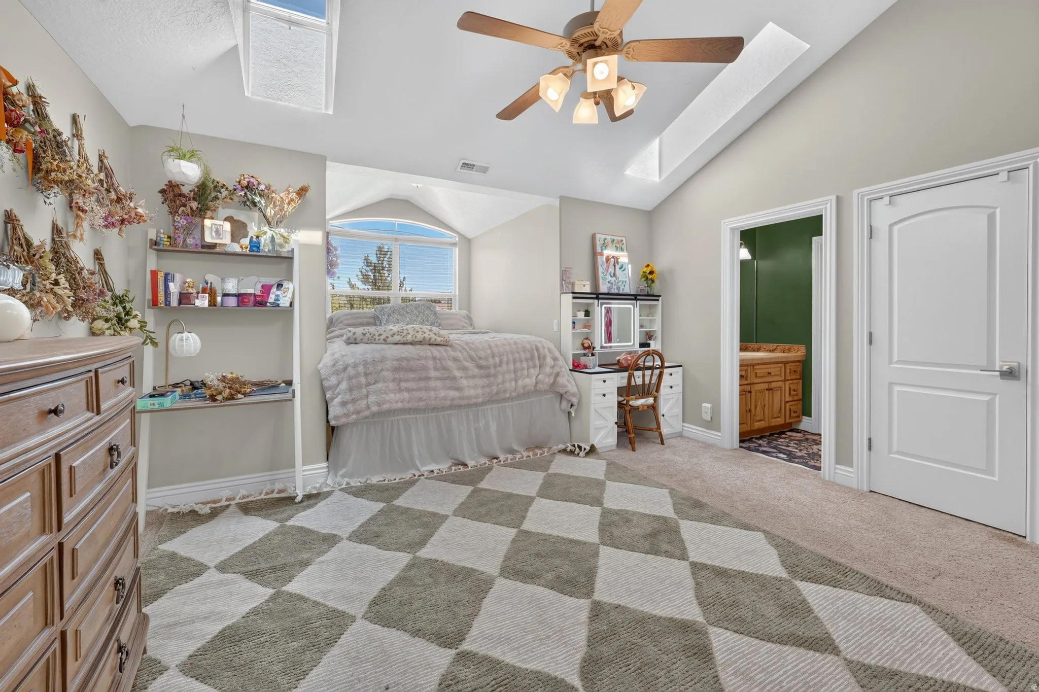 Vaulted ceiling with skylight, ceiling fan, arched window, and wood-finish vanity