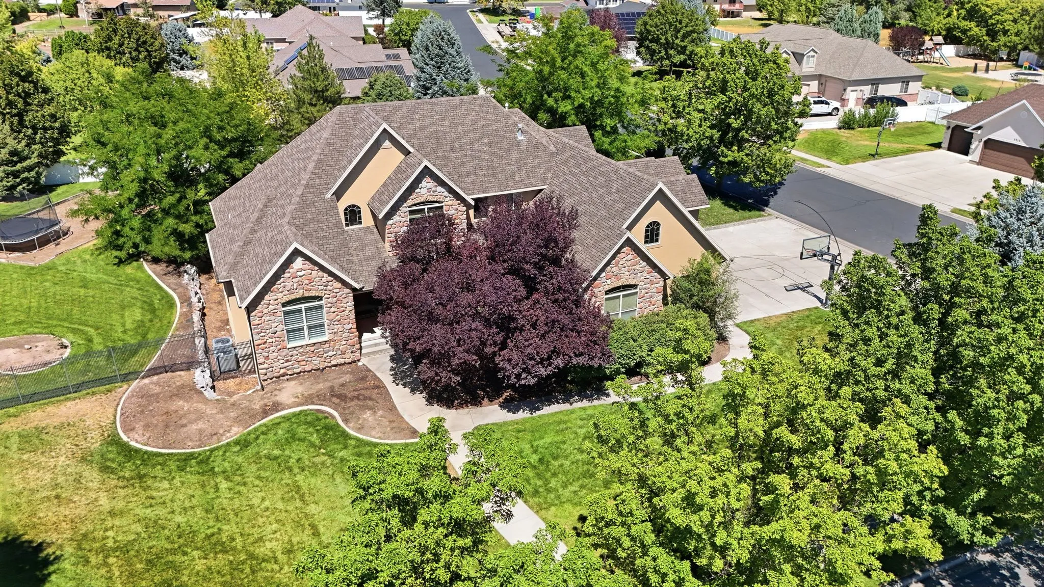 Stone and stucco exterior with multiple gables, extensive landscaping, and concrete driveway