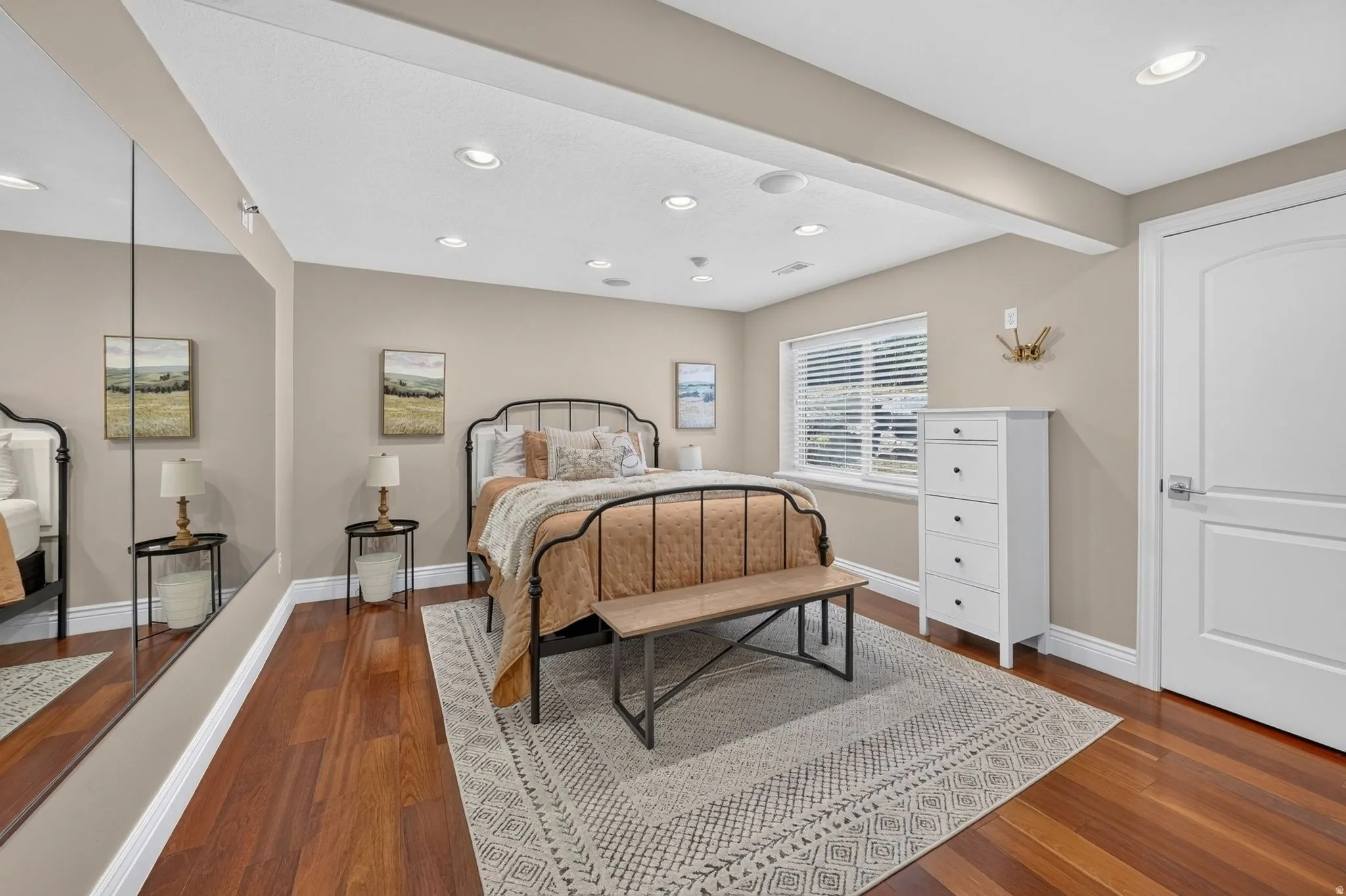 Spacious primary bedroom showcasing hardwood flooring, recessed ceiling lighting, and a metal bed frame