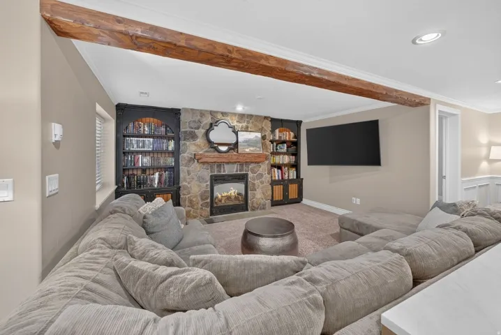 Stone-faced fireplace with a wood mantel, built-in shelving, wood-finish ceiling beam, and recessed lighting