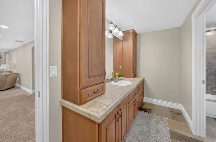 Wood-finish cabinetry with a built-in sink, tile countertop, and matching wall-mounted storage
