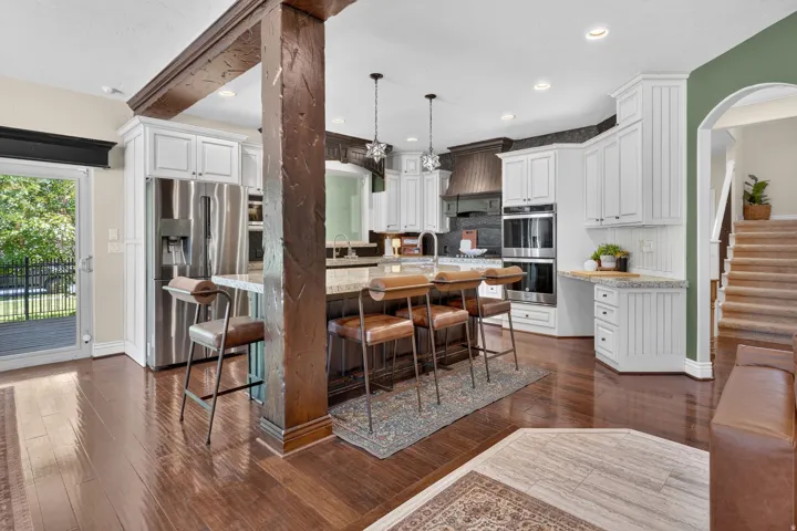 Hardwood flooring, white cabinetry, stainless steel appliances, kitchen island with seating, built-in double ovens