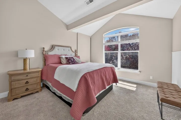 Arched window, vaulted ceiling, light neutral wall paint, carpet flooring, and white wainscoting