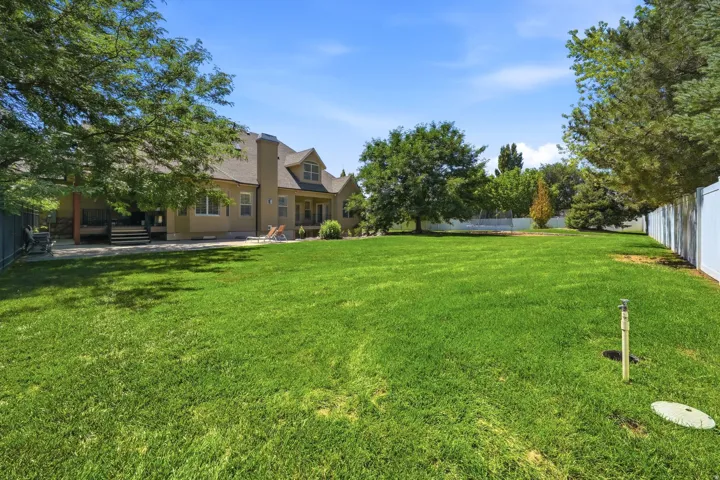 Expansive green lawn with a white privacy fence, mature trees, and a two-story residence with a patio