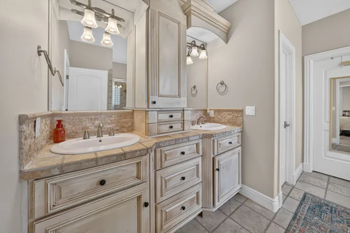 Dual vanity with integrated sinks, distressed wood-finish cabinetry, tile countertops, and a tile backsplash