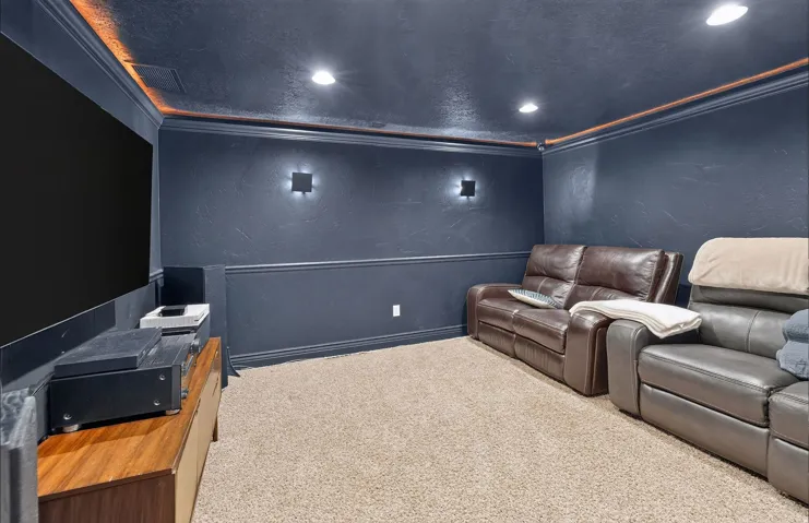 Home Theater featuring dark blue walls with wainscoting detail, recessed ceiling lighting with ambient orange accent trim, plush carpeting, and built-in seating with leather recliners
