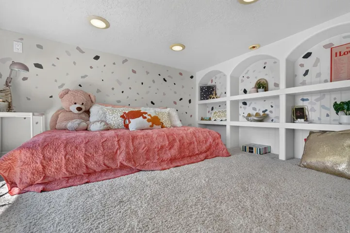 Built-in arched shelving, recessed ceiling lighting, light-colored carpeting, and a decorative accent wall
