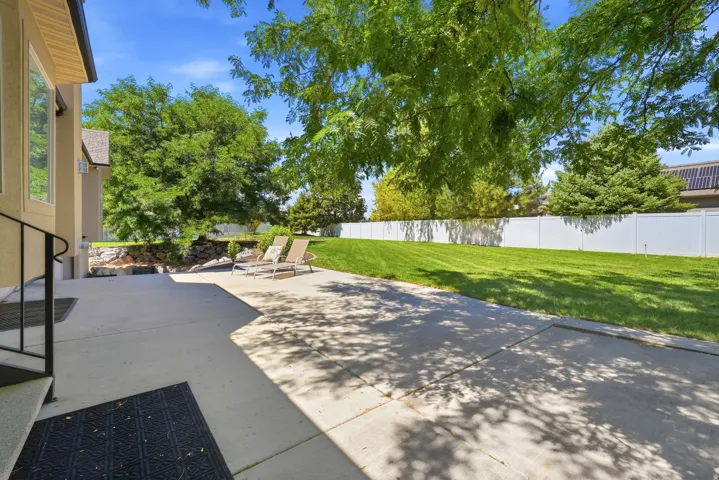 Expansive concrete patio with direct access to a manicured lawn, framed by a white privacy fence and mature trees