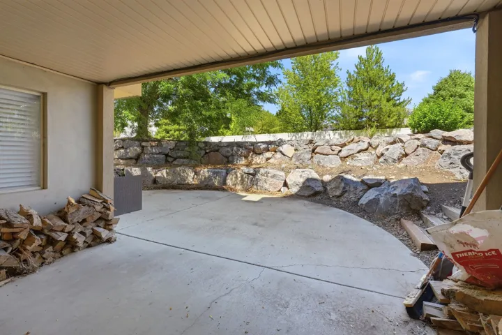Covered concrete patio with a stone retaining wall and surrounding greenery