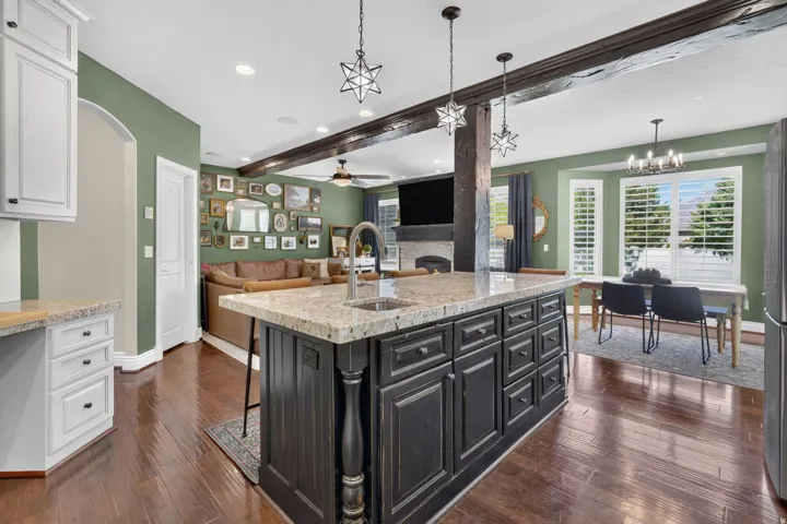 Kitchen island with granite countertop and integrated sink, dark wood-finish flooring, white built-in cabinetry, and exposed wood beams