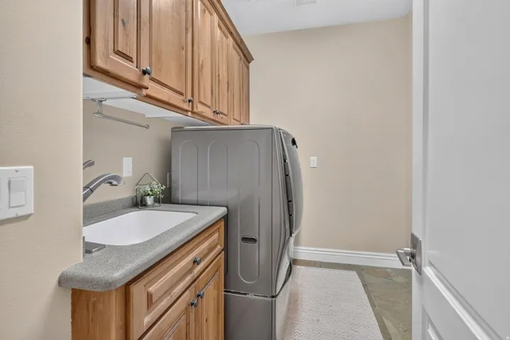 Laundry room with wood cabinetry, a built-in utility sink, and tile flooring