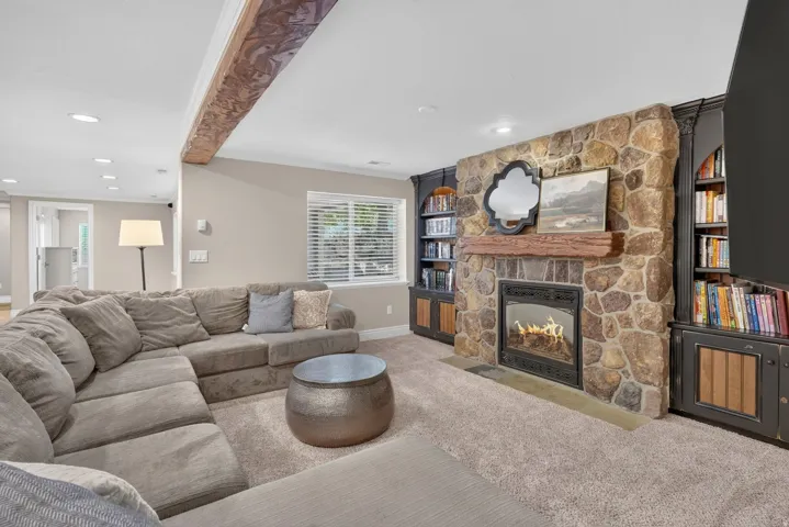 Stone-faced fireplace with a wood mantel, built-in shelving units, and exposed ceiling beam