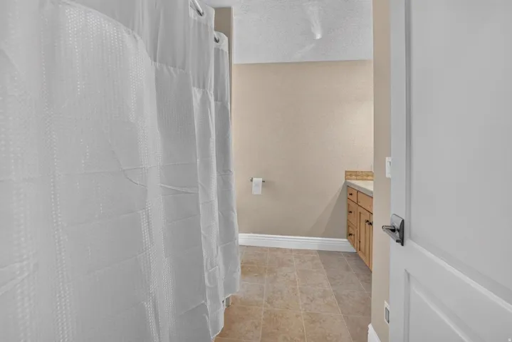 Tile flooring, wood-finish vanity with countertop, and a white interior door with dark hardware