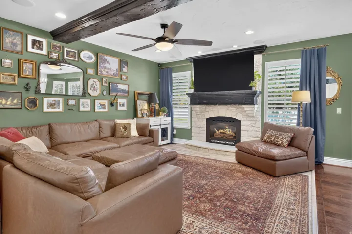 Living room featuring a stone-clad fireplace with a dark wood mantel, exposed ceiling beams, and wood-finish flooring