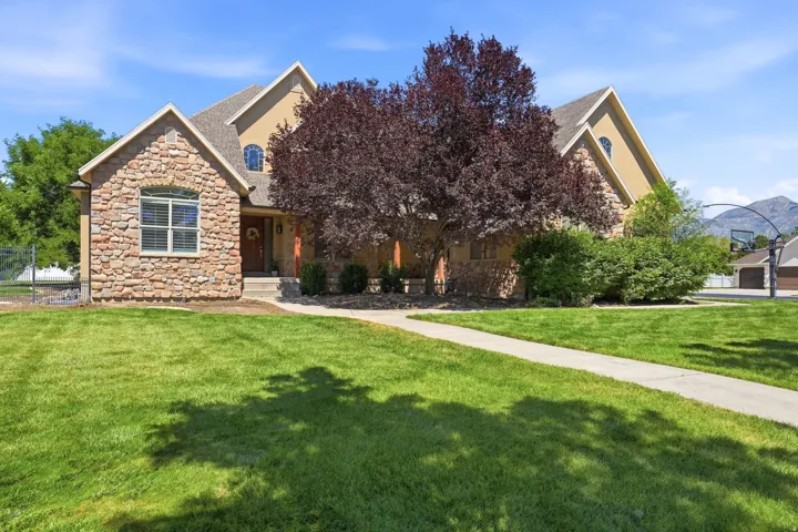 Stone and stucco exterior with arched windows, prominent gables, and an established front yard featuring a concrete walkway