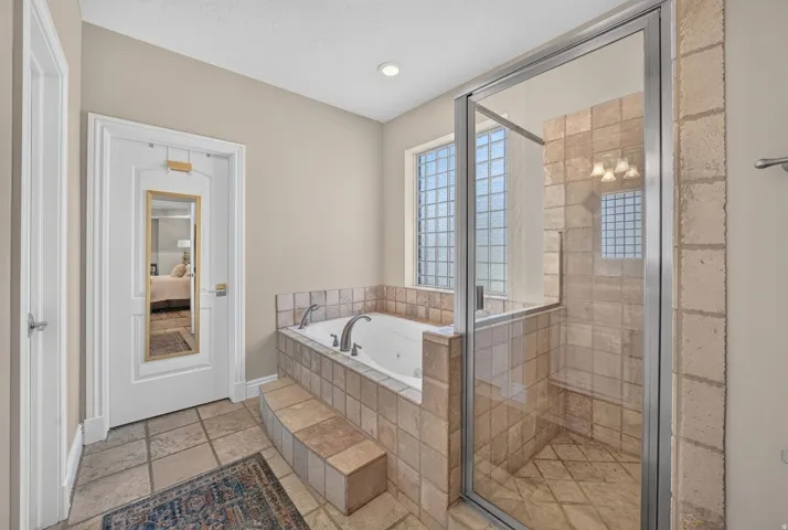 Tiled flooring with a jetted soaking tub, glass-enclosed shower, and recessed lighting