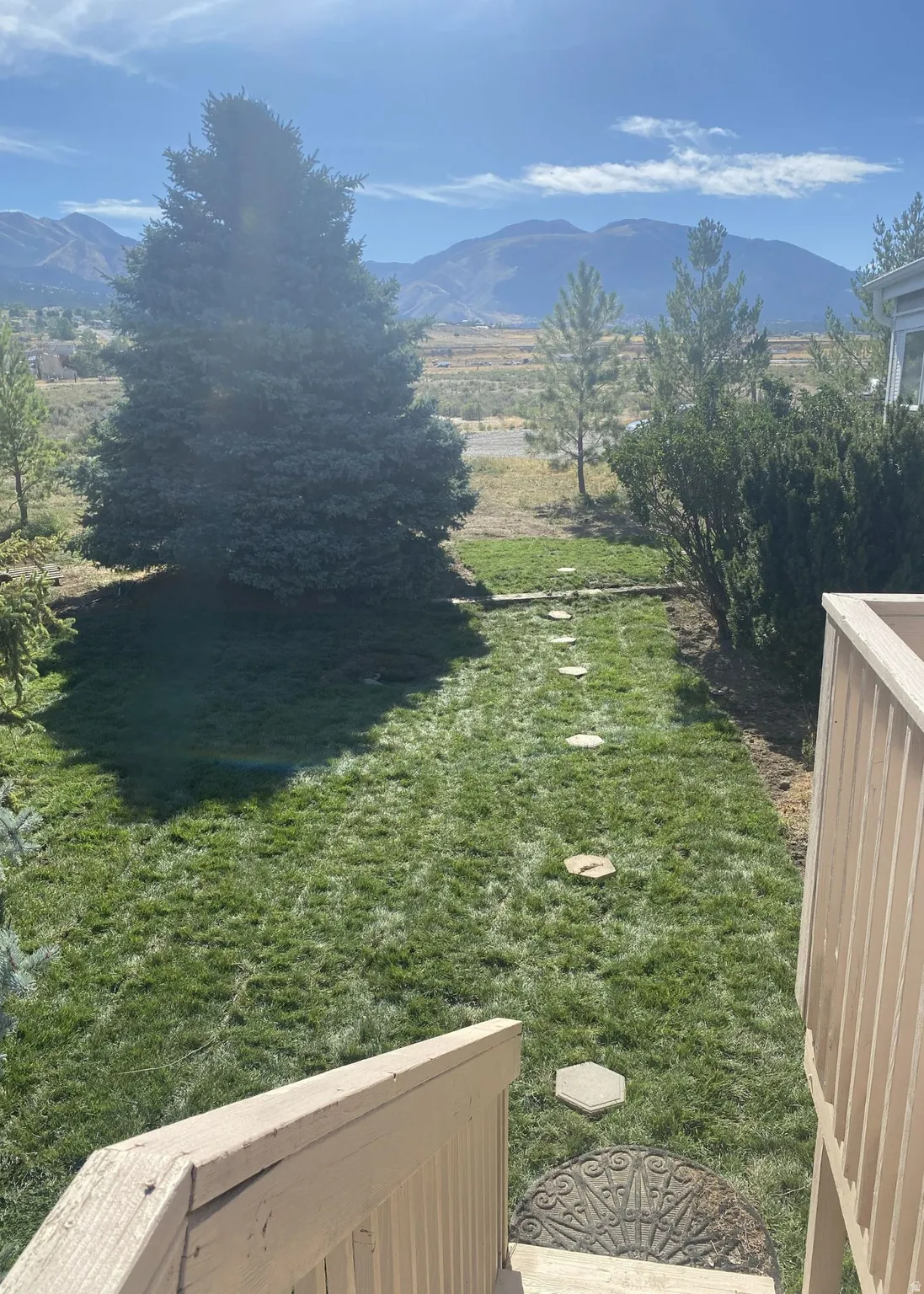 Looking out the front door. Expansive lawn with stepping stone pathway, mature evergreen trees, and distant mountain scenery