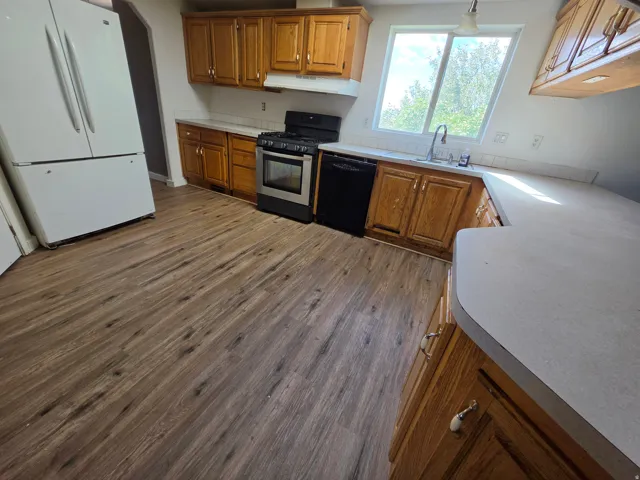 Wood-finish flooring, wood cabinetry, white countertops, built-in dishwasher, and range