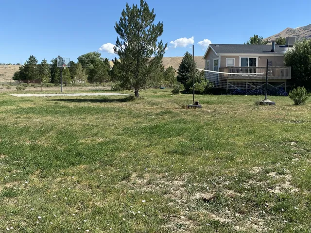 Rear exterior of the home featuring a raised deck with white railing, sliding glass door. Backyard and an adjacent basketball court.
