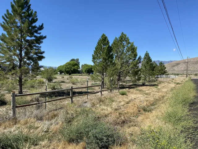 Front of the property with a wood-finish rail fence enclosing a natural landscape with mature trees and mountain backdrop