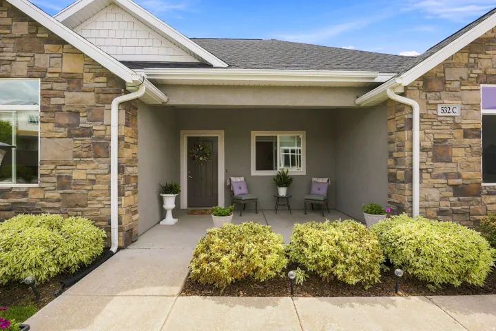 Stone veneer exterior, covered entry, asphalt shingle roof, white gutters, landscaping with shrubs
