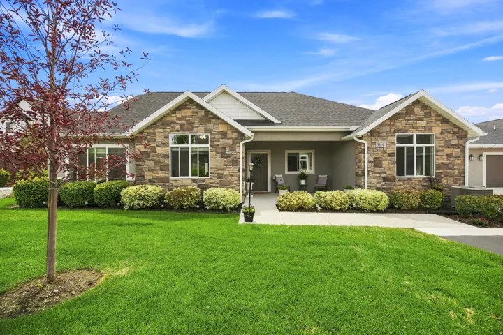 Stone and stucco exterior with a covered entry, established landscaping, and an attached garage