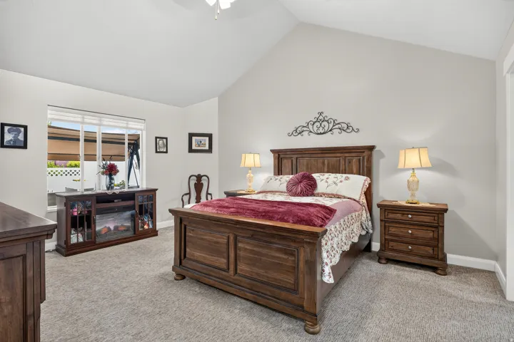 Vaulted ceiling, ceiling fan, large window with blinds, wall-to-wall carpeting, and an electric fireplace feature