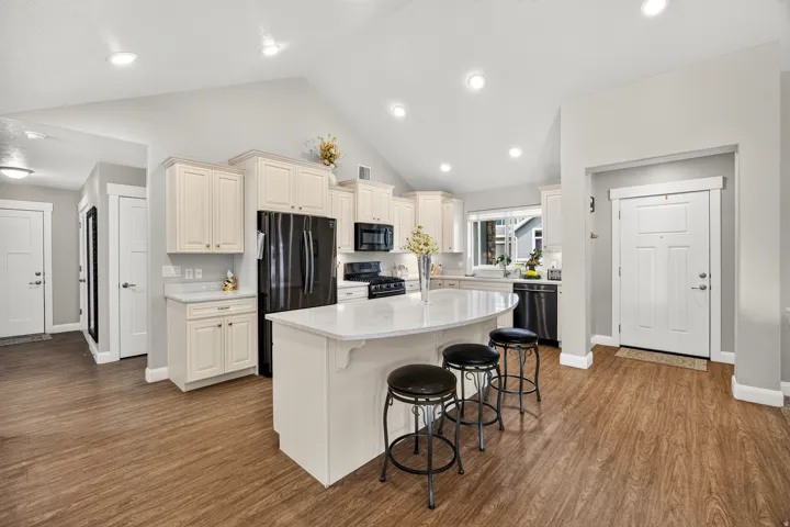 Vaulted ceiling, recessed lighting, wood-finish flooring, white cabinetry, and a kitchen island with seating