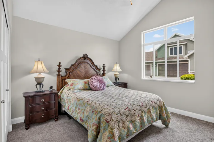 Vaulted ceiling, large window, neutral wall tones, and carpet flooring