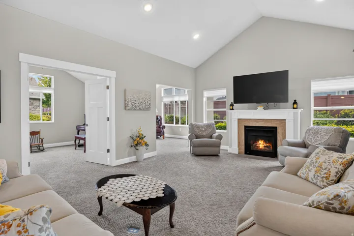 Vaulted ceiling, recessed lighting, gas fireplace with decorative mantel, multiple windows, and a doorway with a three-panel door