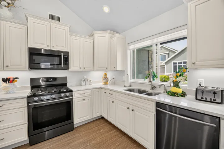 White cabinetry with crown molding, stainless steel appliances, dual basin sink, light-toned countertops, and wood-finish flooring