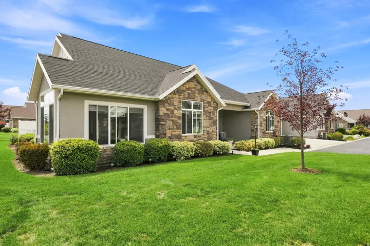 Stucco and stone exterior with large windows, a gabled roofline, and established landscaping