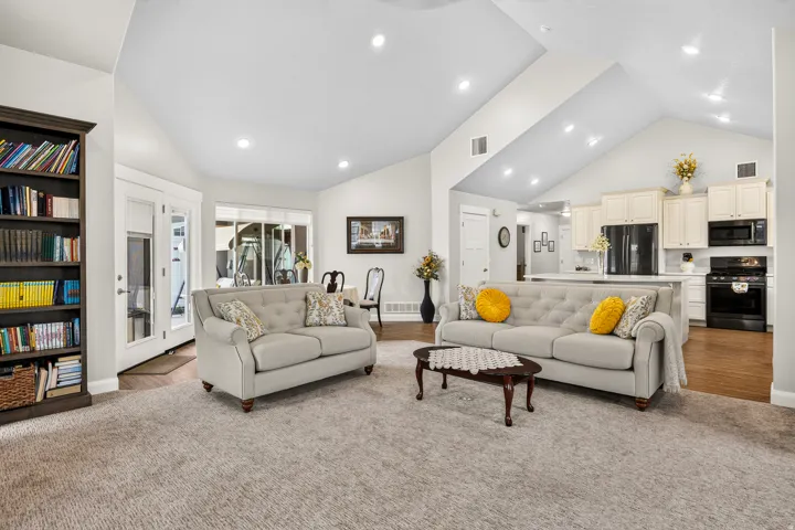 Spacious open-concept living area featuring vaulted ceilings with recessed lighting, hardwood flooring, and two upholstered seating areas anchored by a wood coffee table