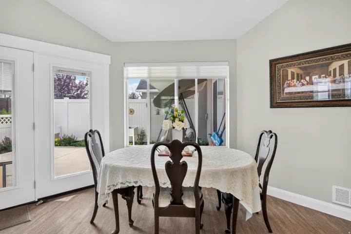 Dining area with wood-finish flooring, light-toned walls, a large window with blinds, and French doors providing outdoor access