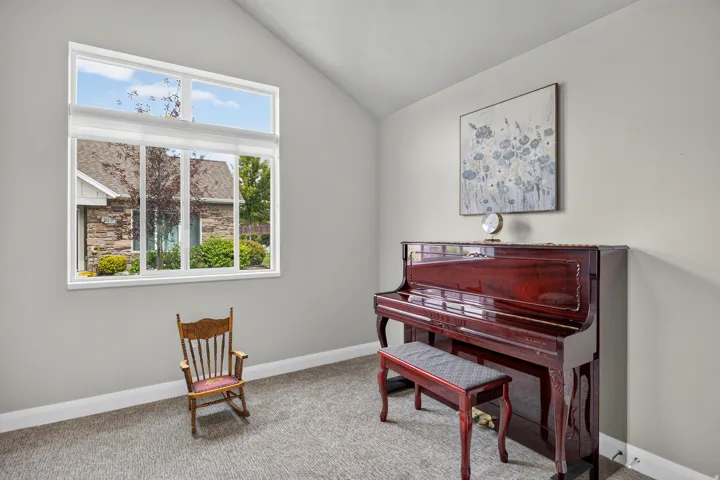 Vaulted ceiling, multi-pane window, neutral wall tones, and gray carpeted flooring