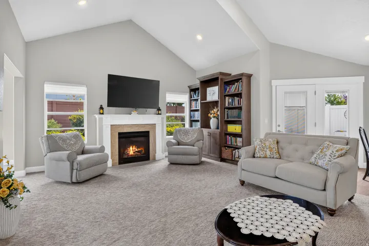 Vaulted ceiling living area featuring a built-in fireplace with a stone surround, multiple windows, and recessed lighting