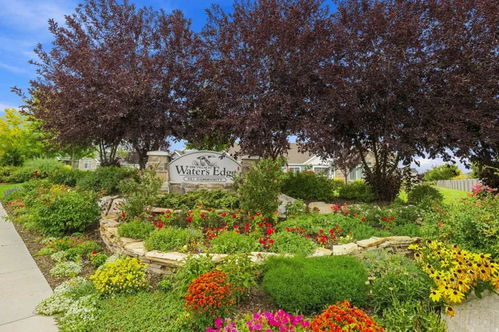 Stone-clad entry sign featuring a natural stone base and lush landscaping with mature trees and vibrant flowering plants