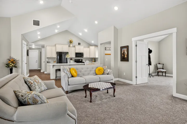 Vaulted ceiling, recessed lighting, white kitchen cabinetry, kitchen island with seating, wood-finish flooring